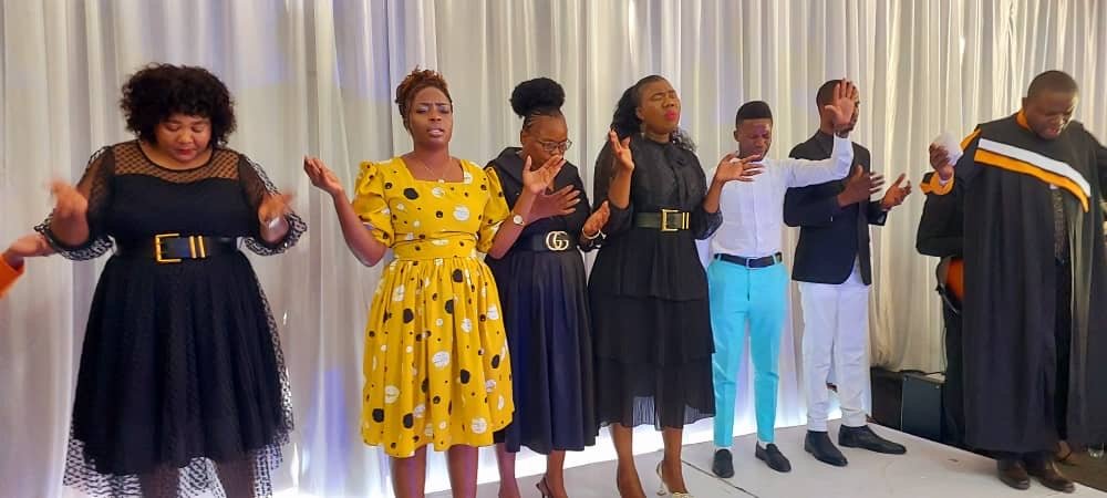 Women and ministers in worship on stage at a TCI assembly
