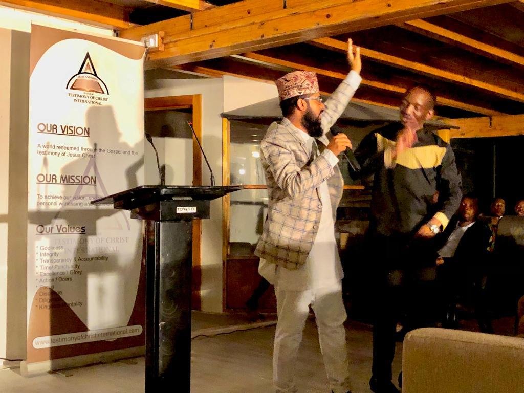 Two ministers preaching together at a TCI gathering, beside the TCI vision, mission and values banner